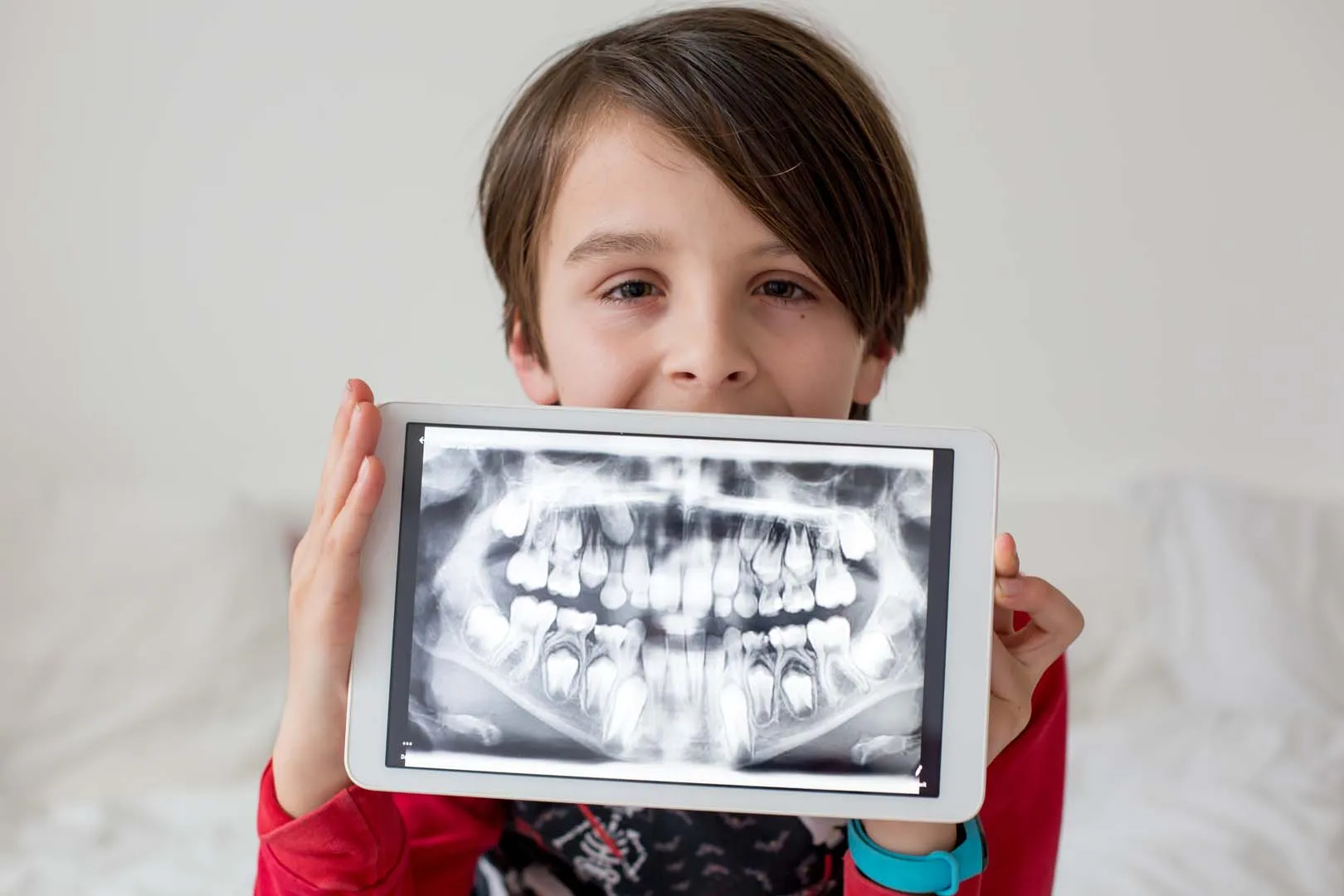 Smiling boy holding a tablet that shows a panoramic X-ray of a child's teeth
